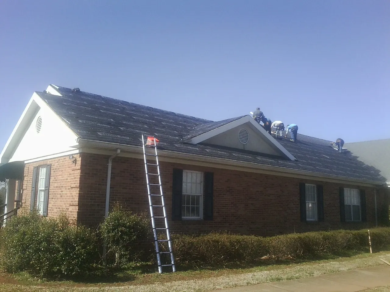 Crew tearing shingles off a brick ranch roof with a ladder set — Metal Roof Repair work by our crew in Murrieta