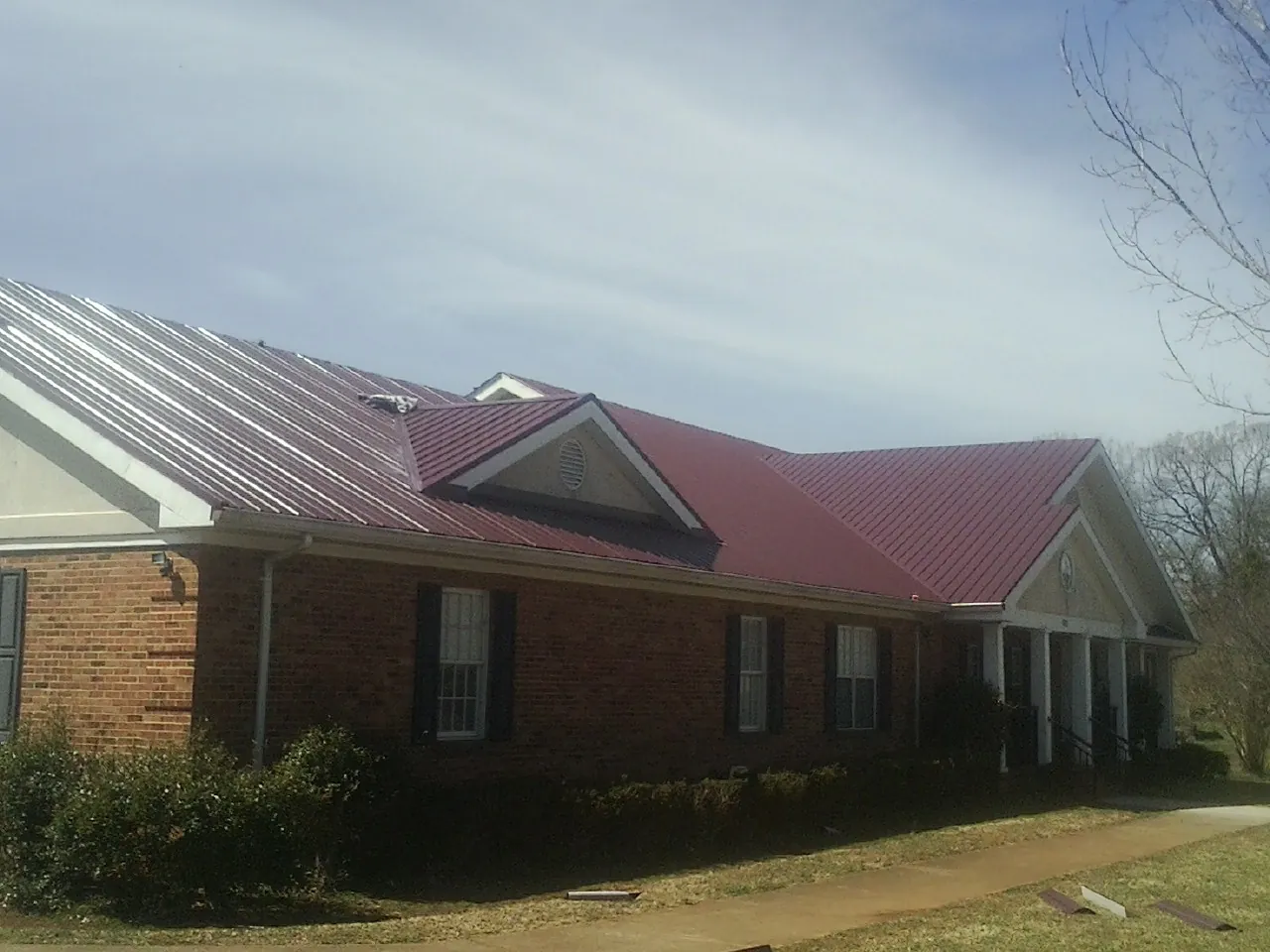Red metal roof with gabled entries on a long brick building, from a Hail Damage Roof Repair job in Murrieta