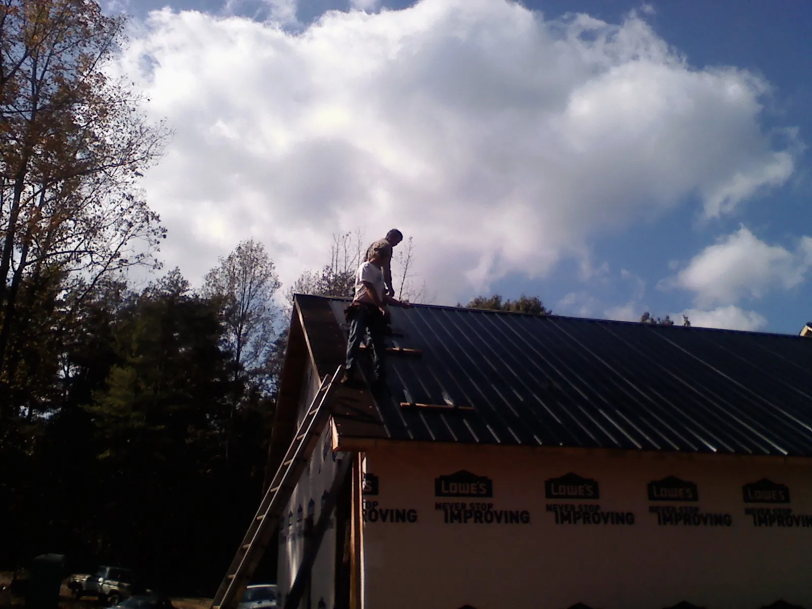 Roofer fastening dark metal panels high against a cloudy sky, from a Roof Inspection job in Murrieta